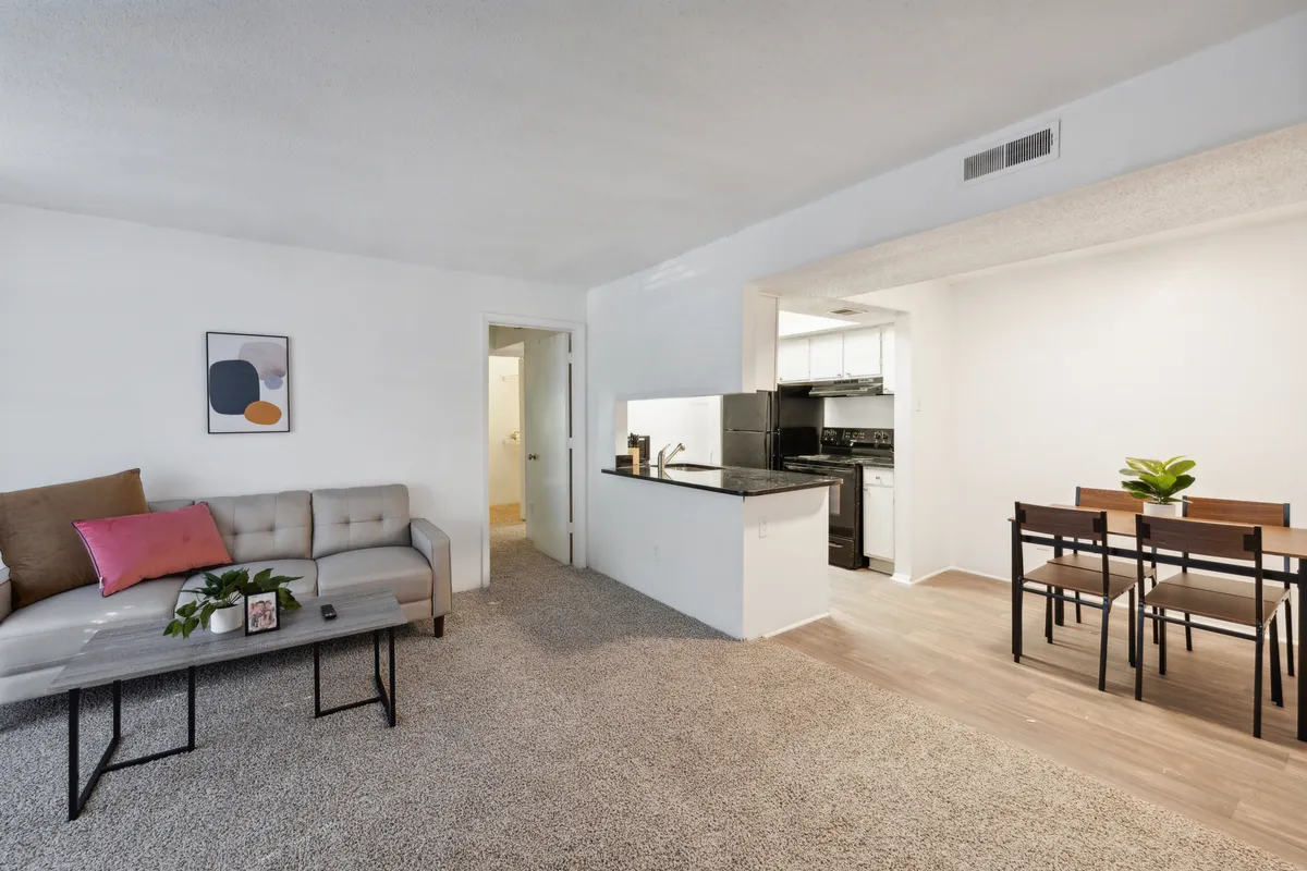 A spacious, open living area featuring a comfortable sofa, a dining table, and a view into the kitchen. Modern decorative artwork brings personality to the space. Natural light streams in, creating a warm and inviting atmosphere ideal for entertaining guests, relaxing, or sharing a meal.