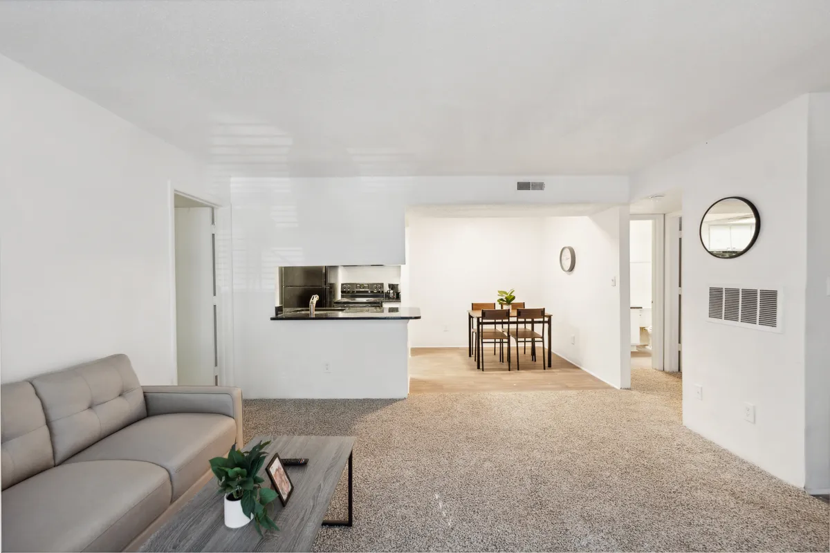 A bright, open-plan living and dining area featuring a comfortable sofa, a dining table set for meals, and a modern kitchen area in the background. The space is well-lit, neatly arranged, and exudes a sense of welcoming comfort, emphasizing the apartment's move-in-ready ambiance.