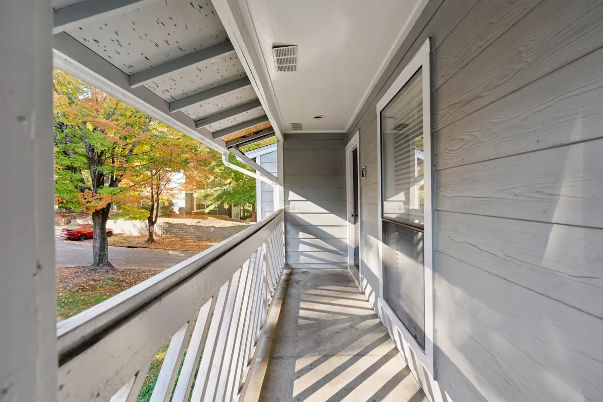 A peaceful exterior shot highlighting the porch railing, the door leading into the residence, lush tree views, and a sidewalk that hints at the walkable, inviting surroundings. The scene suggests an easy connection to the outdoors and the nearby neighborhood.