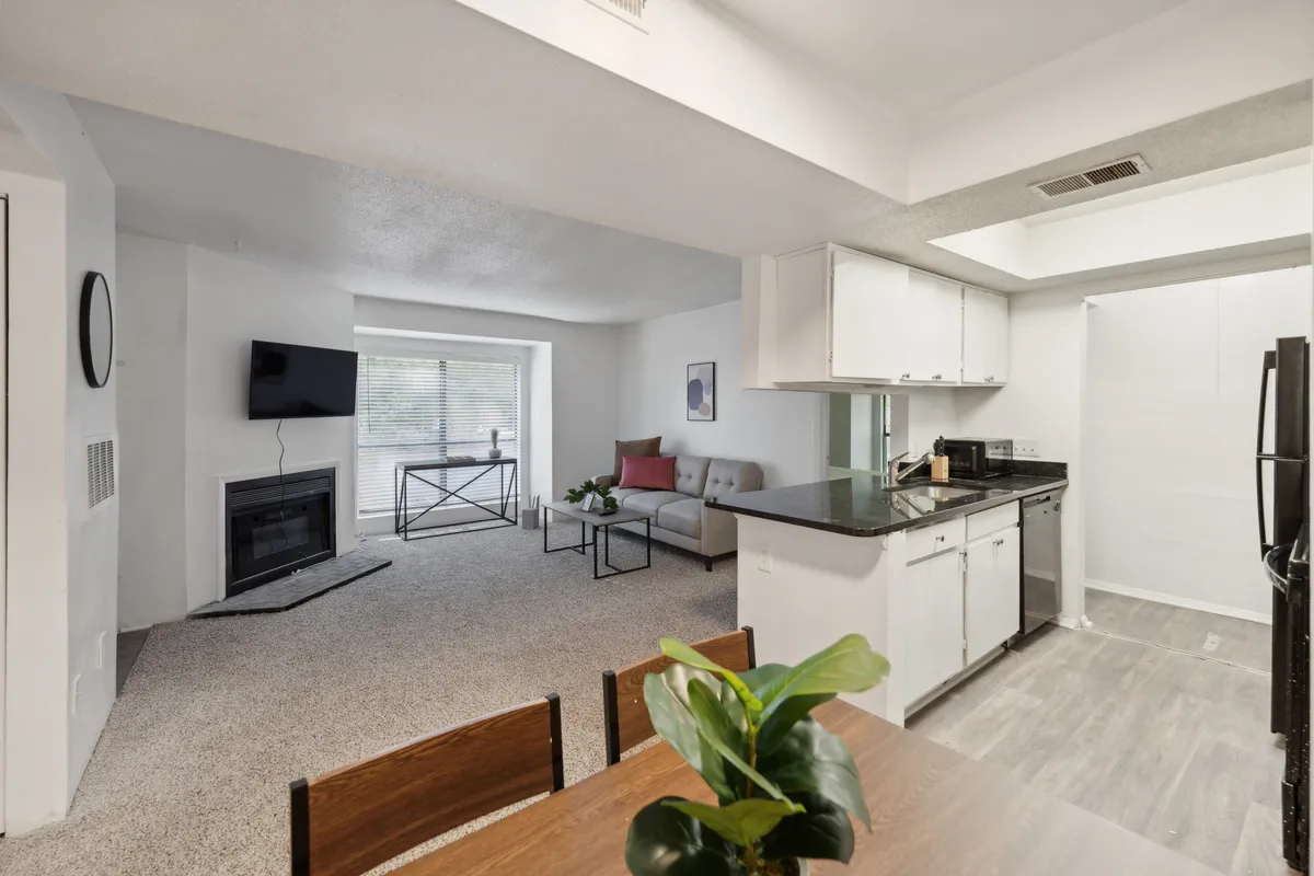 This image captures an inviting, open-plan living space with a visible kitchen counter, a comfortable sofa, and a dining table. The kitchen area is seamlessly connected to the lounge, highlighting the open design and the ease of entertaining or enjoying meals together. The decor is modern and cozy, with clean lines and plenty of space for both cooking and relaxing.