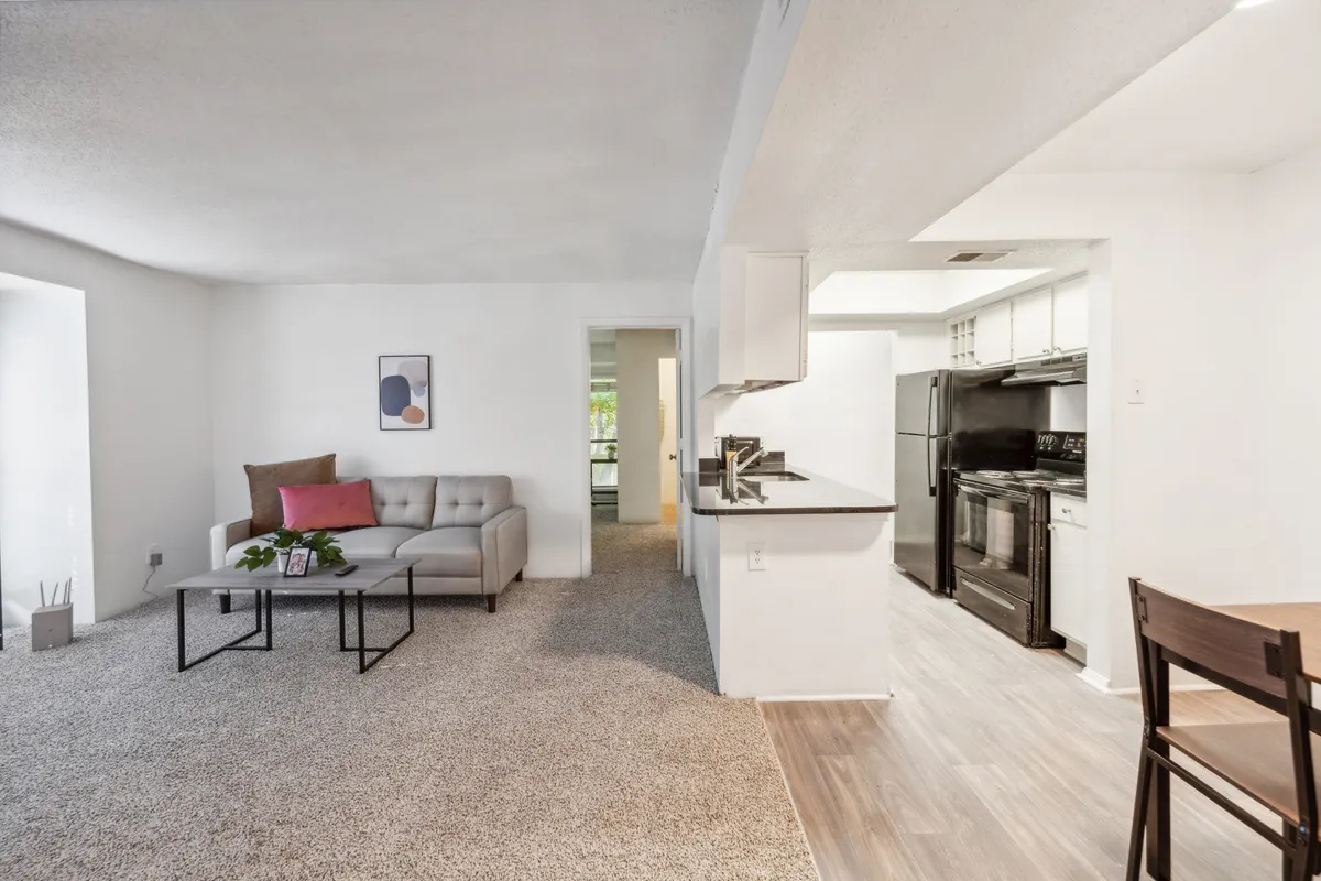 A welcoming view of a living room with a plush sofa, adjacent kitchen area, and a dining table. The space feels intimate yet open, with soft lighting and cozy design elements that invite relaxation and socializing.