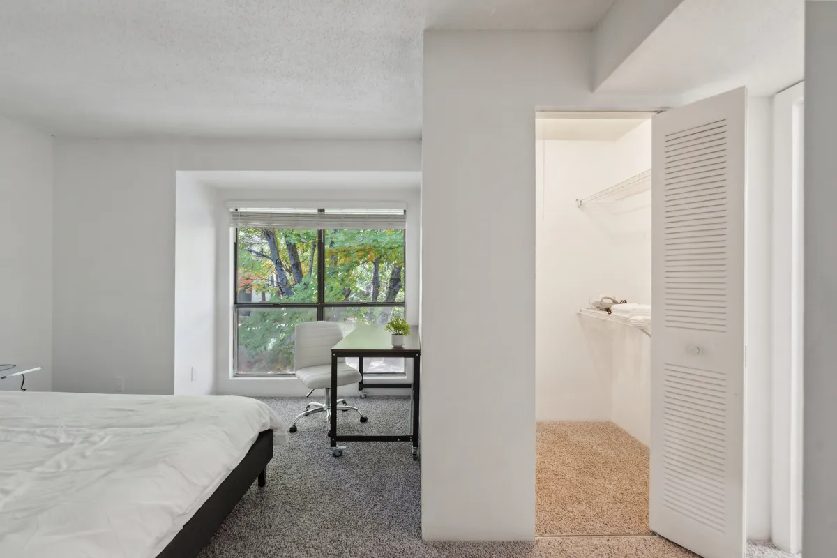 A tranquil bedroom scene complete with a neatly made bed, large window bringing in natural light, a work desk, and chair. The space is thoughtfully arranged for both restful sleep and productivity, reflecting the dual needs of professionals and families.