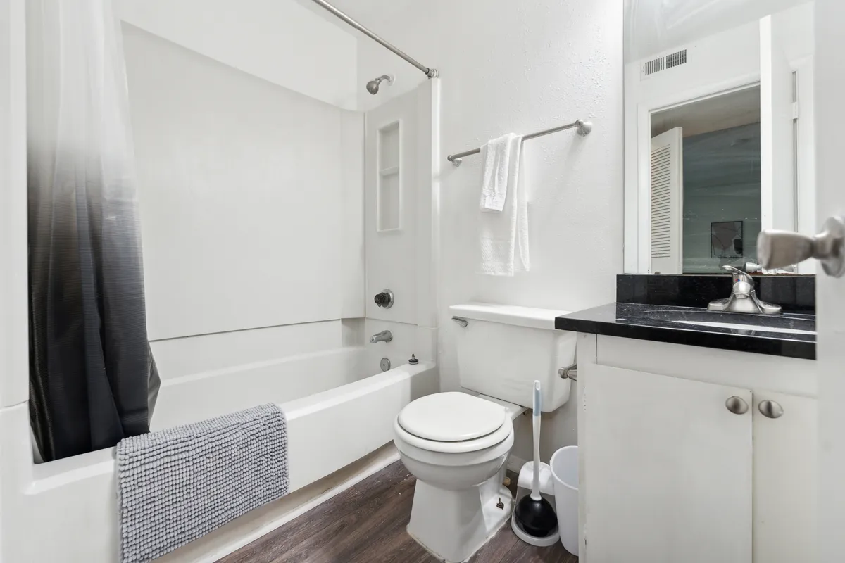 This image features a modern, fresh bathroom with a bathtub, sink, toilet, and mirror. The space is brightly lit and inviting, designed for relaxation and convenience—ideal for both quick routines and calming baths.