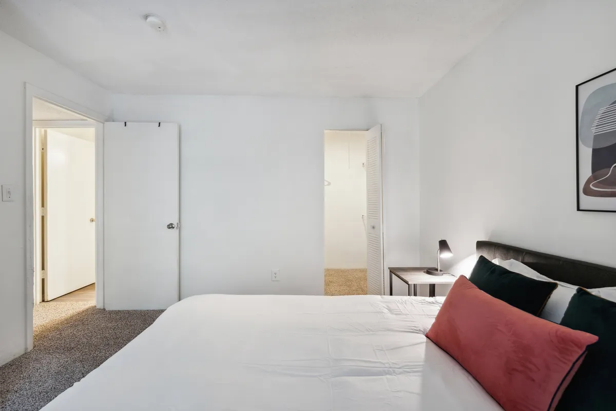 A serene bedroom scene showcasing a neatly made bed with decorative pillows, a nightstand, and tasteful artwork on the wall. The atmosphere is tranquil and inviting, highlighting the comfort and thoughtfulness of the apartment's furnishings.