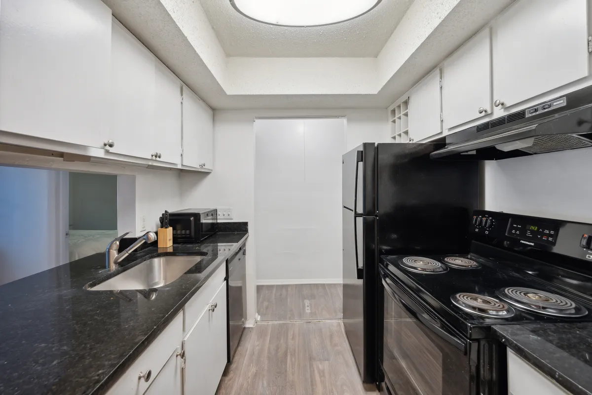 A close-up view of the kitchen highlights striking black appliances, a sleek granite countertop, and crisp white cabinetry. The layout is practical and inviting, with ample prep space and modern amenities, conveying both style and full functionality.