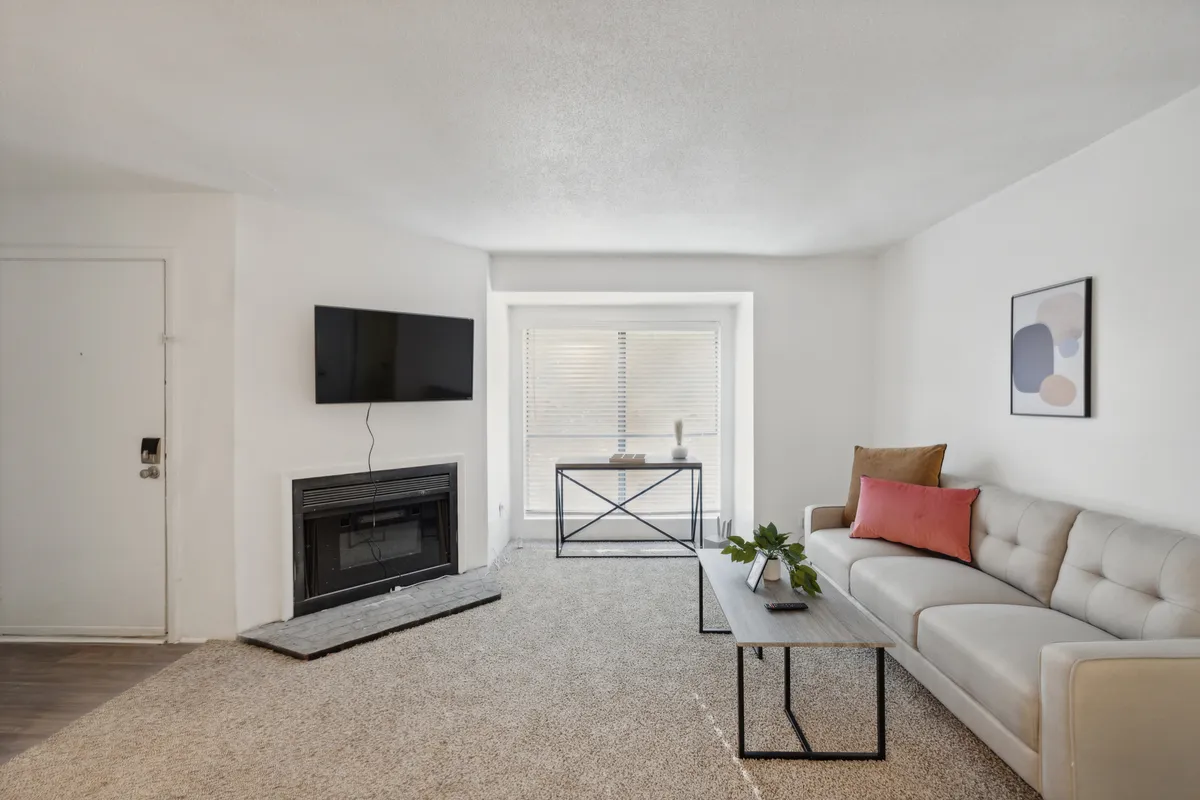 A cozy living room setup featuring a large sofa, coffee table, fireplace, television, and a window that lets in abundant sunlight. The room feels both bright and inviting, perfect for unwinding or connecting with others.