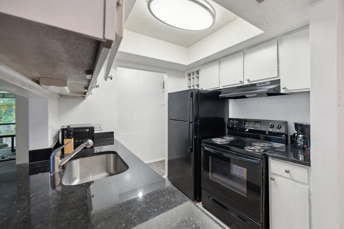 Another angle of the kitchen, featuring matching black appliances, expansive granite countertops, and white cabinetry. The scene conveys an atmosphere of modern comfort, ideal for cooking together or hosting family meals.